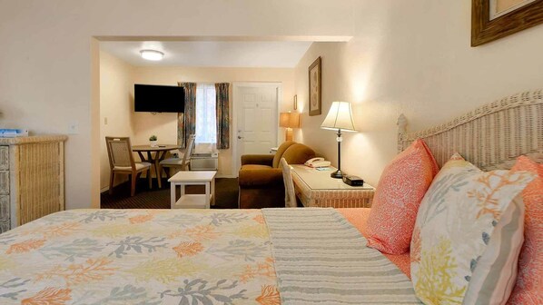 A hotel room with a bed, a desk, a chair, a television, and a lamp.