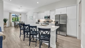 A modern kitchen with white cabinets, stainless steel appliances, and a central island with bar stools. - Luxe Canal Home, Boat Rental, Walk to Cape Harbour (Cape Coral)