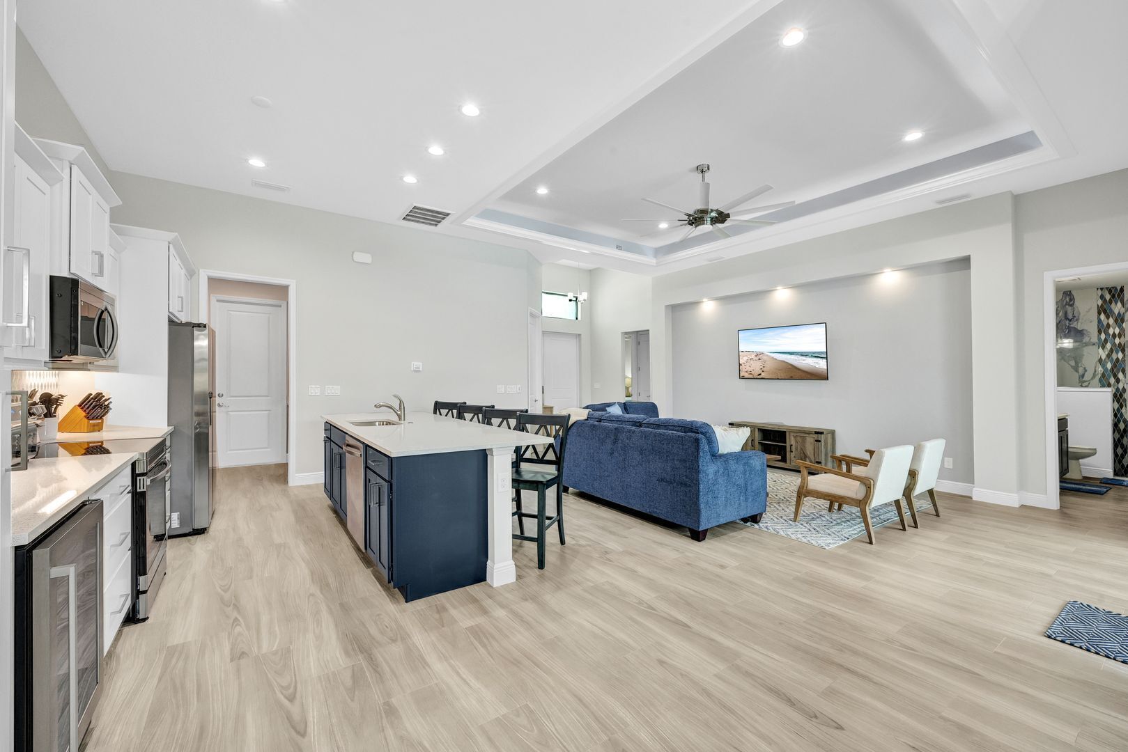 A modern kitchen with white cabinets, a central island, and a dining area with a blue sofa.