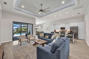 Un salon spacieux avec un canapé bleu, une table basse en bois et une vue sur une piscine et un espace extérieur.