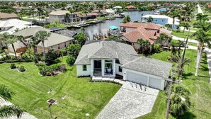 A residential area with a house featuring a large front yard, a garage, and a dock extending into a body of water. - Luxe Canal Home, Boat Rental, Walk to Cape Harbour (Cape Coral)