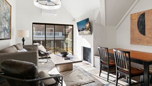 A spacious living room with a modern chandelier, a fireplace, and a dining area with a wooden table and chairs.