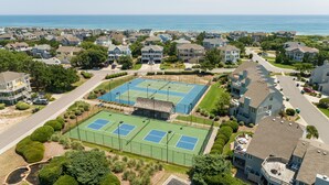 Uma área residencial com quadra de tênis, rodeada por casas, uma praia e uma vista clara do oceano.