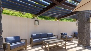 Ein möblierter Patio-Bereich im Freien mit einer Pergola, einer Steinsäule und einer Sitzecke mit Sofas und Sesseln.