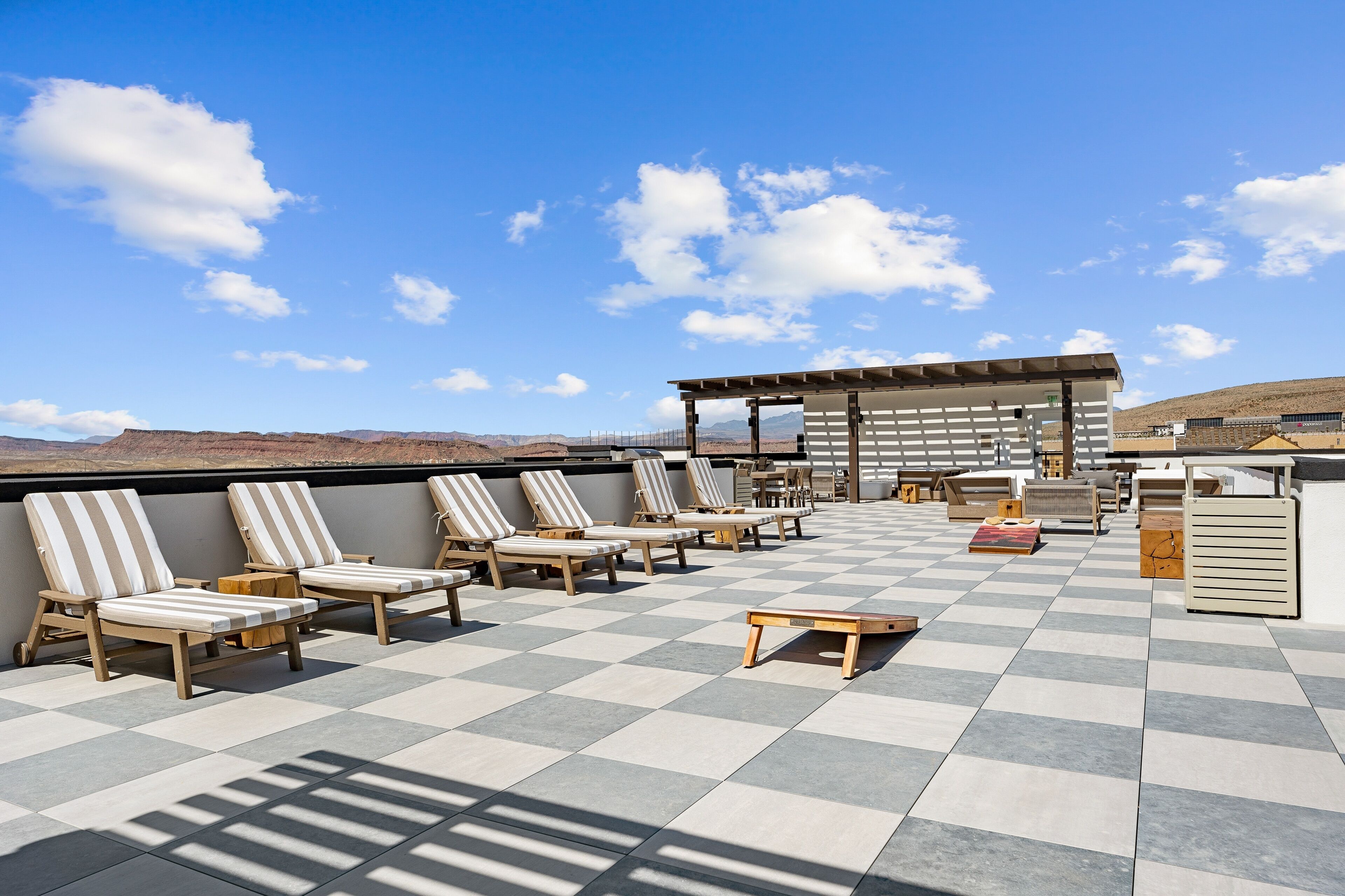 Terraza en la azotea con sillones a rayas, piso a cuadros y una pérgola.