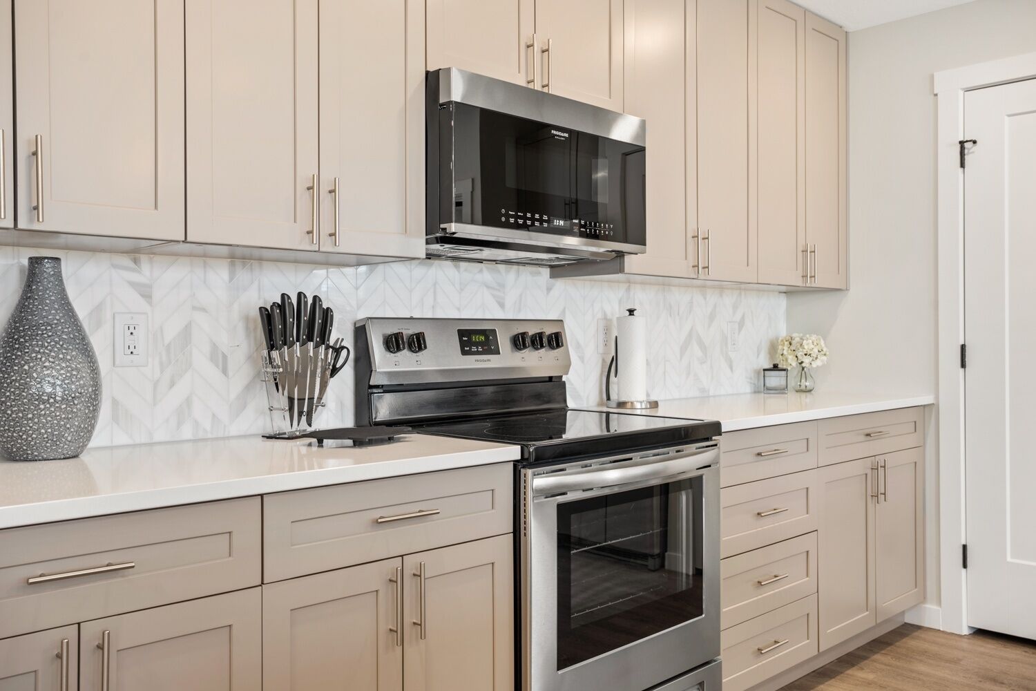 Una cucina moderna con elettrodomestici in acciaio inossidabile, mobili beige e un piano di lavoro bianco.