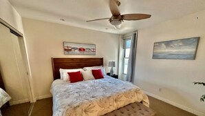 Un dormitorio con una cama, ventilador de techo, ventana y obras de arte en las paredes.