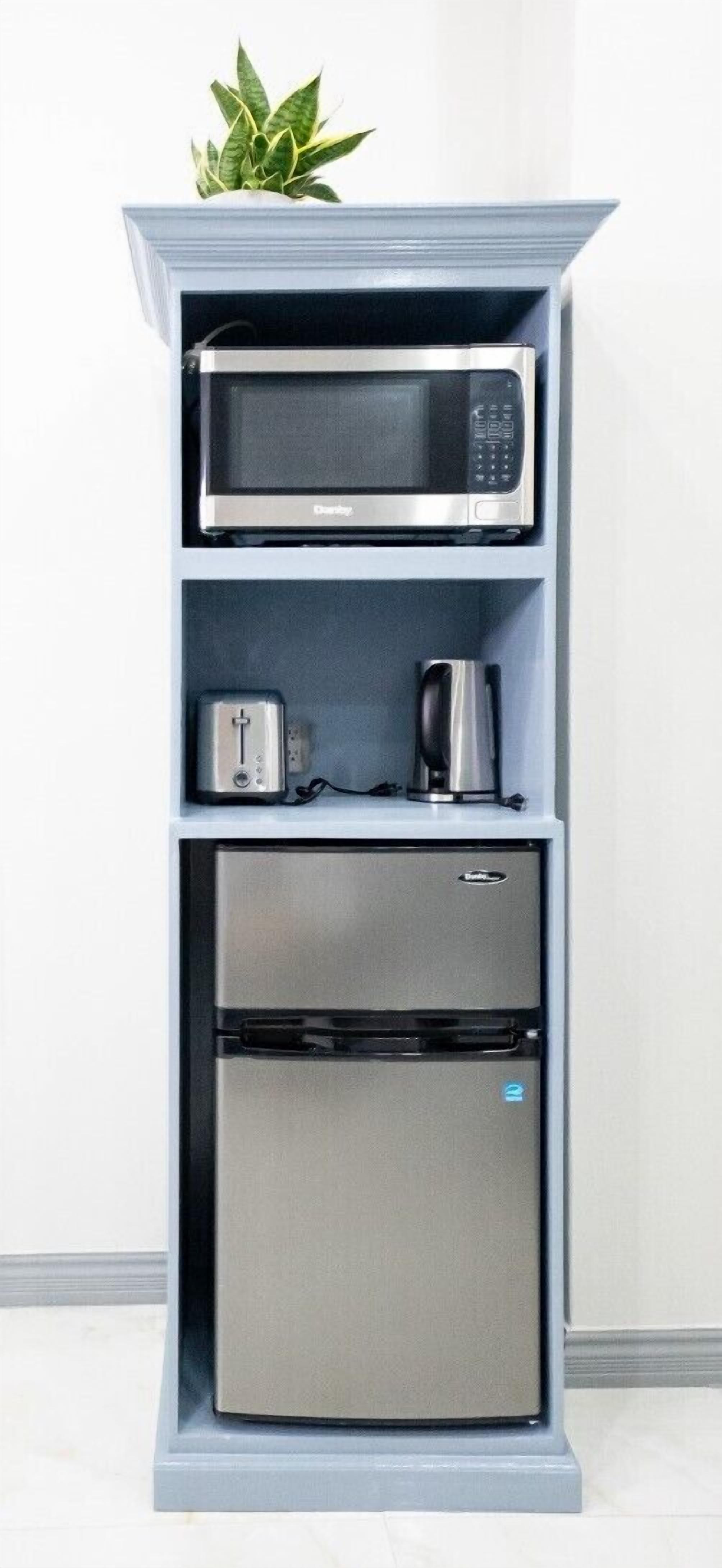 A kitchenette with a microwave, toaster, and coffee maker on a shelf, and a refrigerator below.