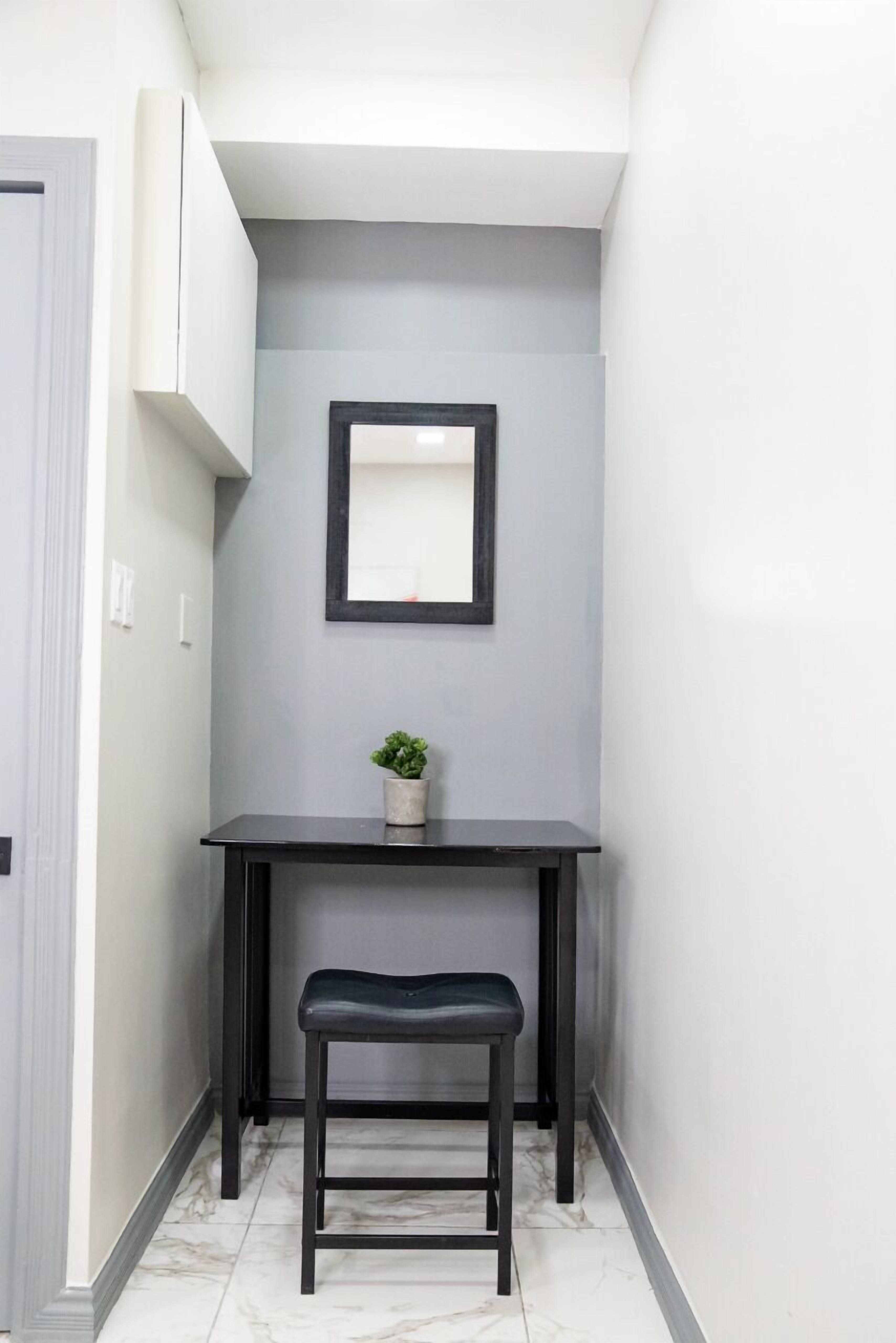 Un pasillo estrecho con un escritorio y un banco de madera oscura, una pequeña planta en maceta y un espejo enmarcado en la pared.