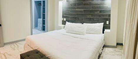 A bedroom with a bed, a nightstand, a wardrobe, and a headboard with built-in lighting.
