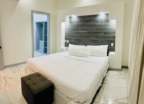A bedroom with a bed, a nightstand, a wardrobe, and a headboard with built-in lighting.