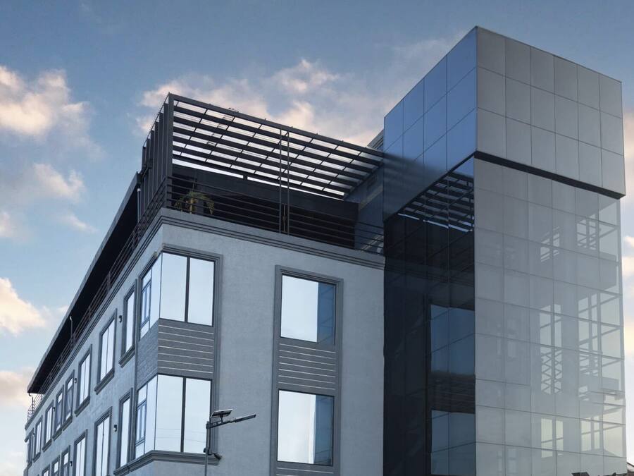 A modern building with a glass facade, large windows, and a flat roof with a metal structure.