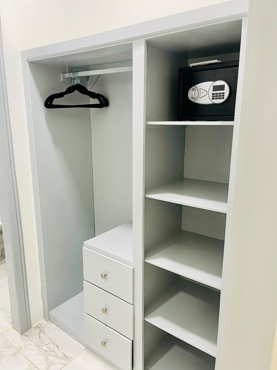 Une armoire blanche dotée de nombreuses étagères et de tiroirs, d’une tringle pour suspendre les vêtements et d’un coffre-fort.