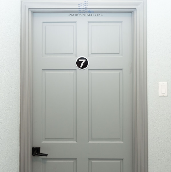 Una puerta blanca con un letrero con el número 7, un picaporte y una placa encima que dice "592 HOSPITALITY INC.".