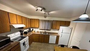 A compact kitchen with wooden cabinets, a white stove, a dishwasher, and a dining table. - Stay Anchorage! Fully Furnished Apartments with GCI RED 2 GIG Internet (Anchorage)