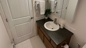 A bathroom with a white door, a sink, a mirror, a towel rack, a plant, and a toilet. - Stay Anchorage! Fully Furnished Apartments with GCI RED 2 GIG Internet (Anchorage)
