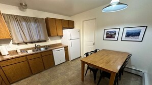 A compact kitchen with wooden cabinets, a white refrigerator, a dishwasher, and a dining table with chairs. - Stay Anchorage! Fully Furnished Apartments with GCI RED 2 GIG Internet (Anchorage)
