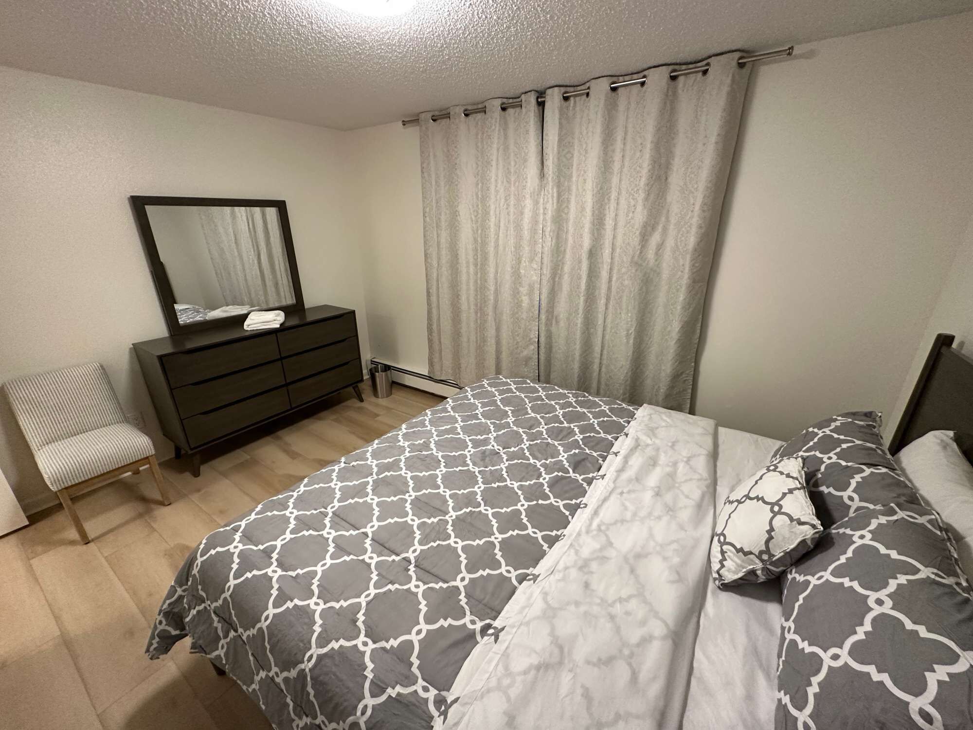 A bedroom with a bed, a dresser, a chair, and a mirror.