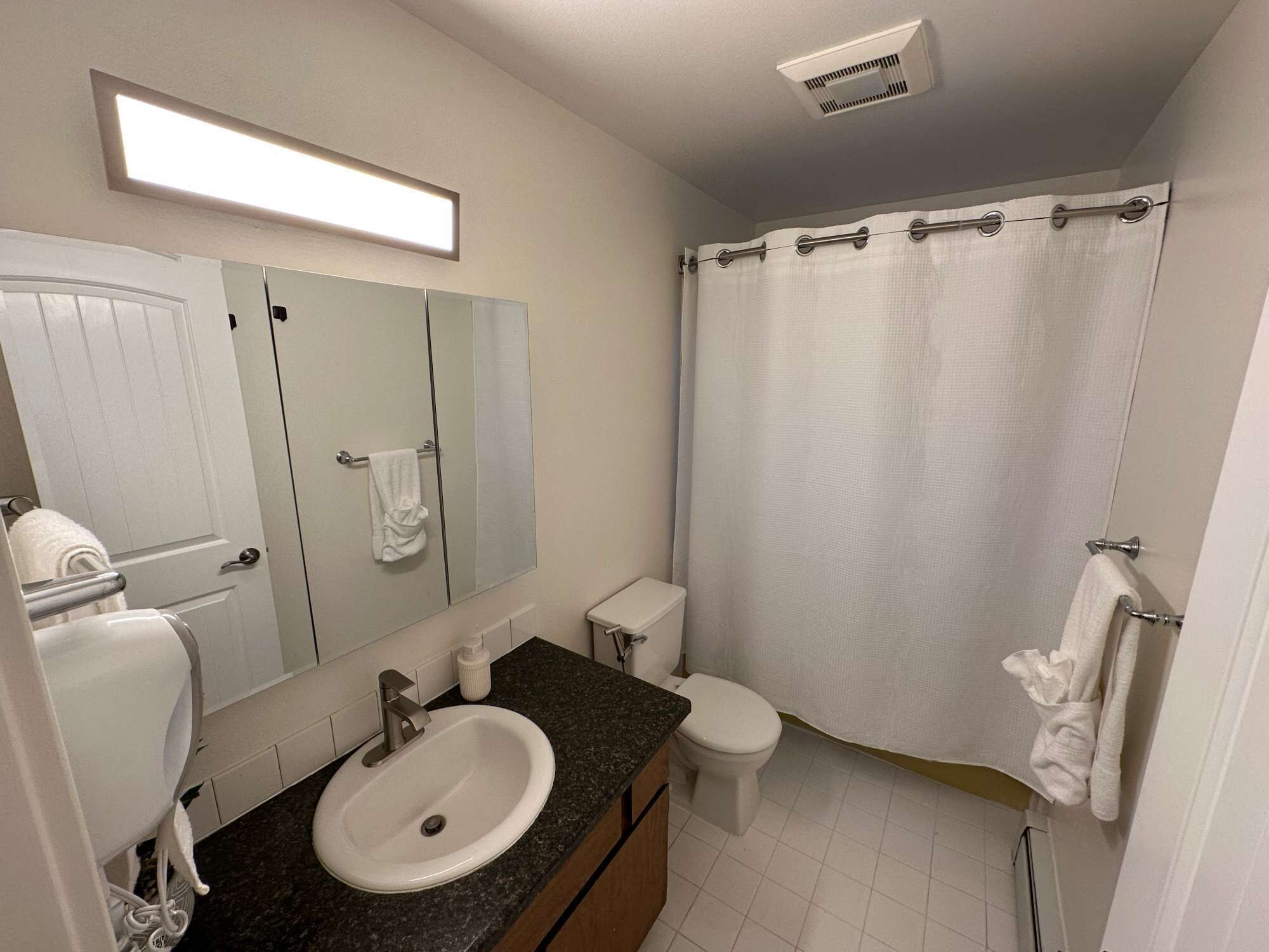 Un baño moderno con lavamanos, espejo, inodoro y cortina de ducha blancos.
