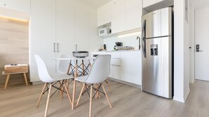 Eine moderne Küche mit weißen Schränken, einem Edelstahl-Kühlschrank und einem Essbereich mit weißen Stühlen und einem Holztisch.