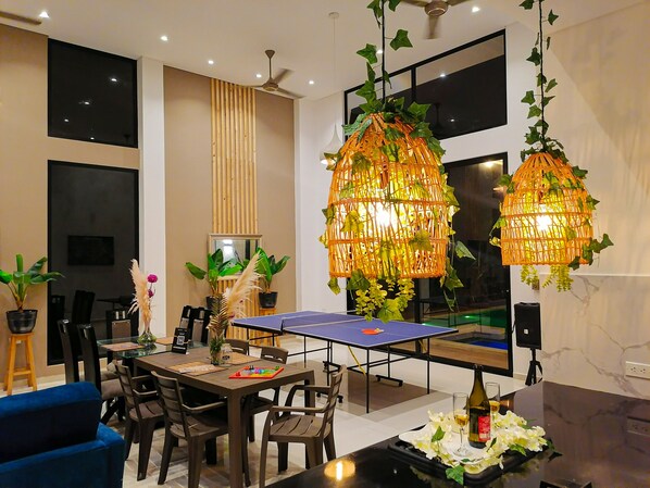 A modern dining area with a ping pong table, wooden chairs, and a blue sofa.