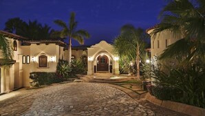A stone-paved courtyard with a central archway, surrounded by palm trees and well-lit by wall-mounted lights. - Villa de Lujo en Cabo del Sol Casa Costa (Cabo San Lucas)