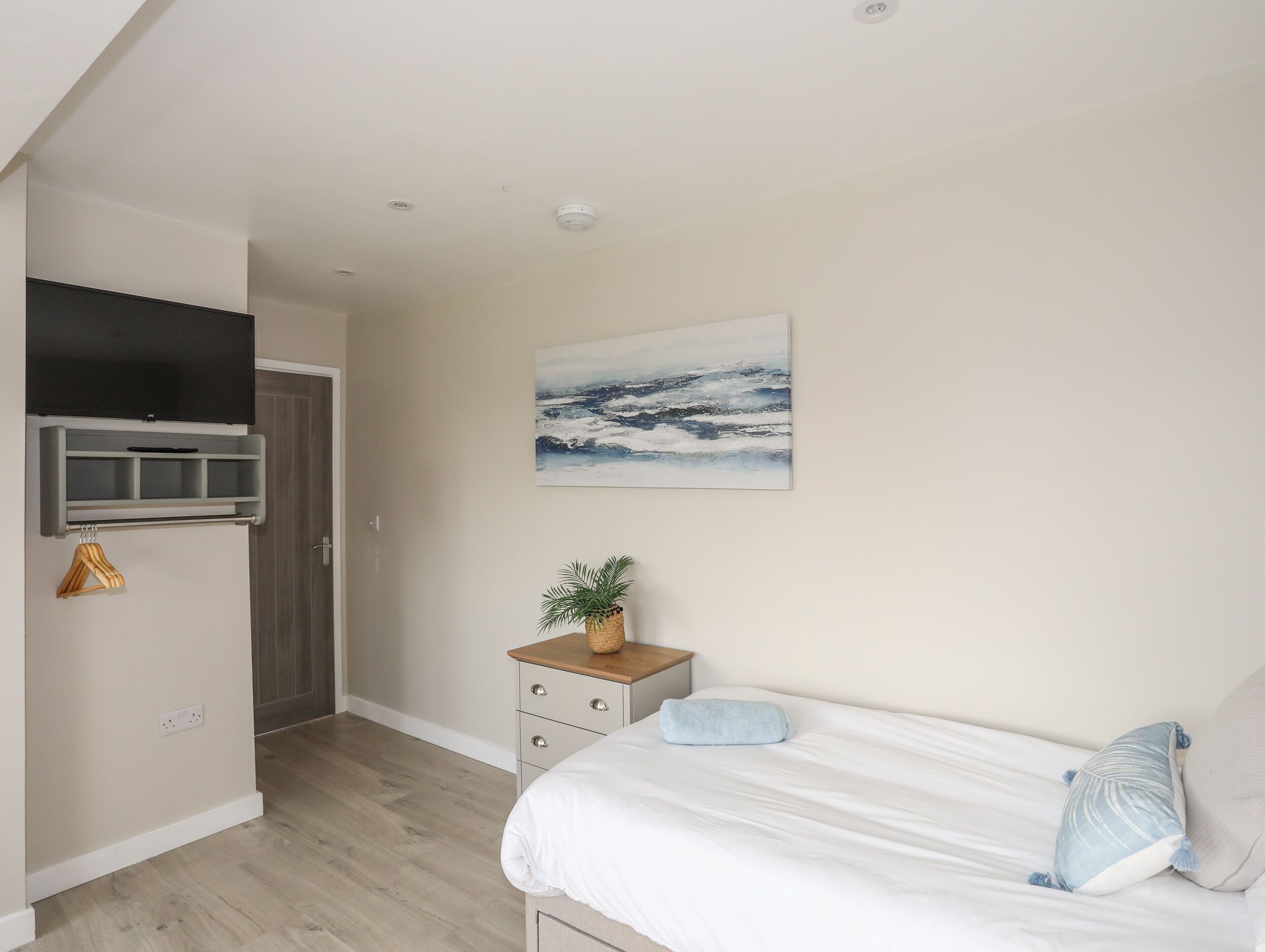 A bedroom with a bed, a nightstand, a wall-mounted TV, a painting, and a plant.