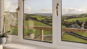 Una ventana con vistas a un paisaje rural, que incluye campos, una carretera y colinas lejanas.