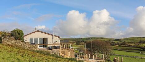 A modern house with a stone wall, a wooden deck, and a view of rolling hills.