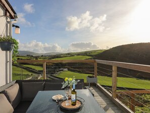 A balcony with a table set for a meal, a bottle of wine, and a view of rolling hills and a valley. - Bryn Y Mor (Tywyn)