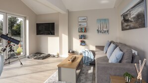 Una sala de estar moderna con un telescopio, un televisor de pantalla plana, una estantería y un cuadro.