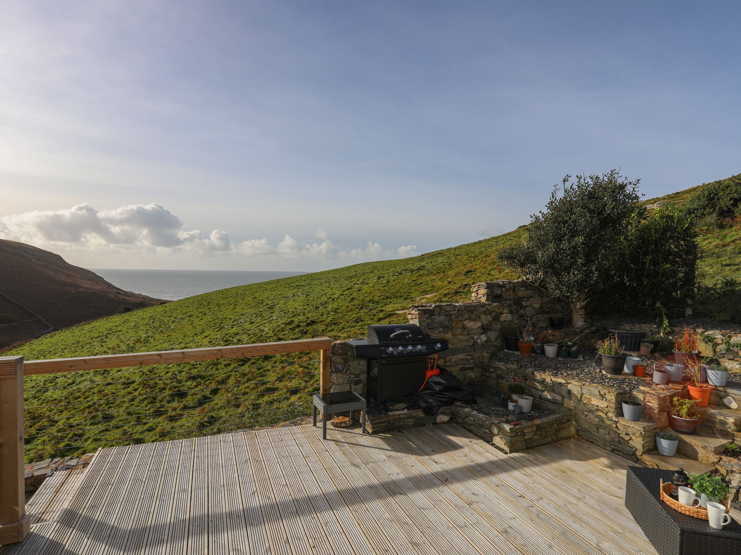 A wooden deck with a stone wall, a barbecue grill, and potted plants.