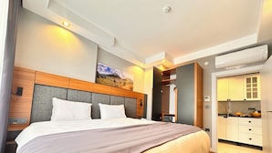 Moderni hotellihuone, jossa on suuri sänky, sängynpääty, jossa on sisäänrakennettu valaistus, taulu seinällä ja näkymä keittiötilaan.