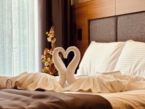 A bed with a heart-shaped towel arrangement, a floral decoration, and a neutral-toned headboard. - Golden Inn Airport Trabzon (Trabzon)