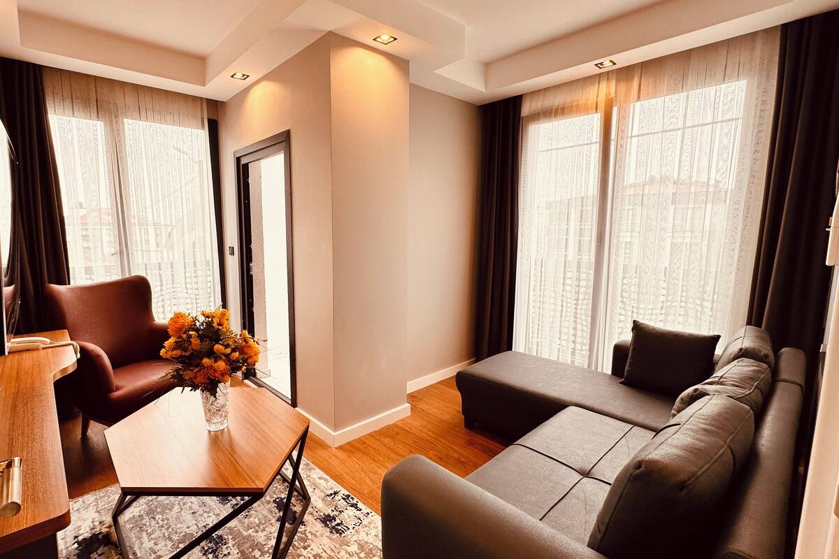 A modern living room with a sofa, armchair, and coffee table. There is a television on a stand and a door leading to another room.