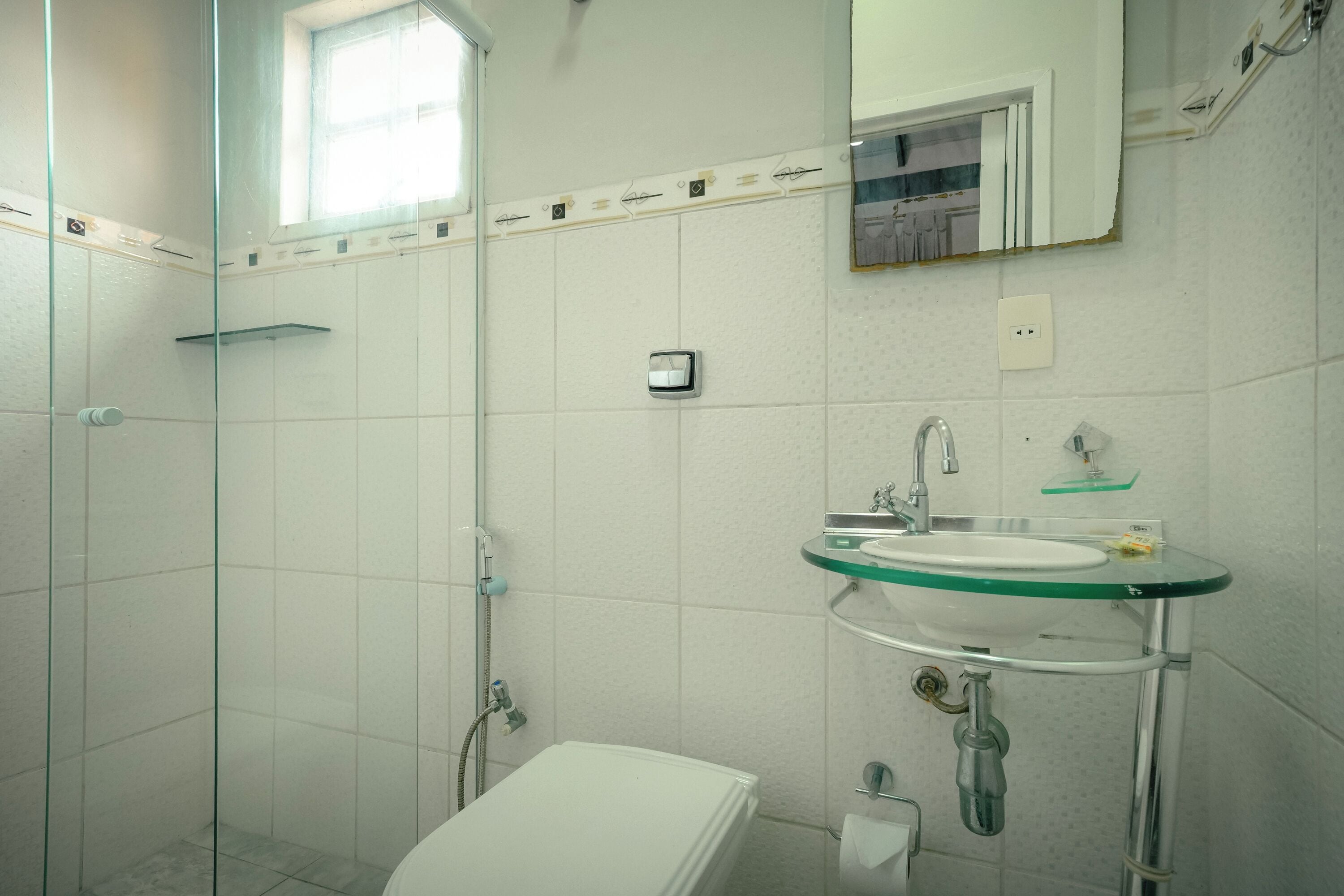 A bathroom with a glass shower enclosure, a white toilet, a sink with a glass basin, and a mirror above the sink.