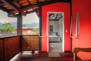 A room with a wooden floor, a bed with a white bedspread, and a view of mountains through an open doorway. - VELINN Pousada Face Norte (Ilhabela)