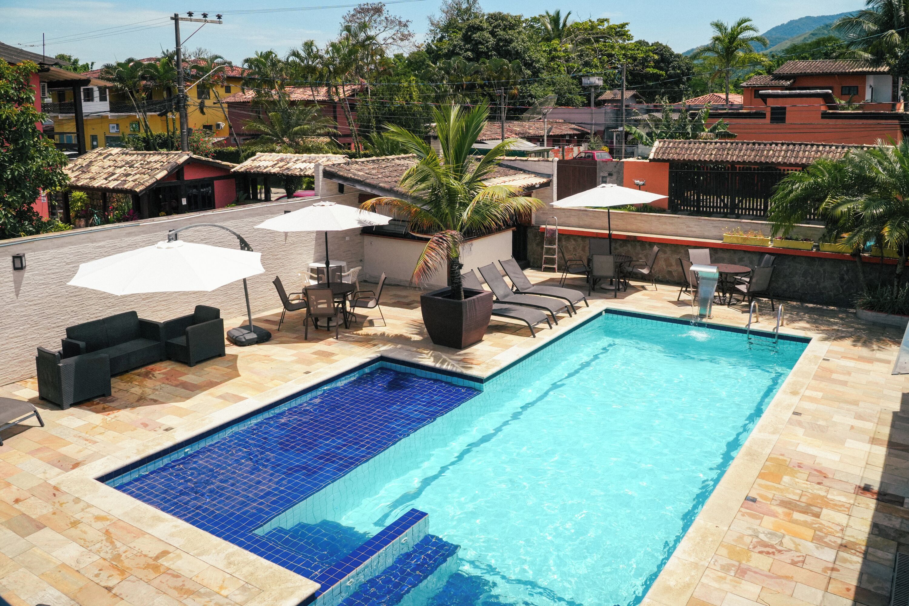 A rooftop swimming pool with tiled flooring, lounge chairs, and umbrellas.