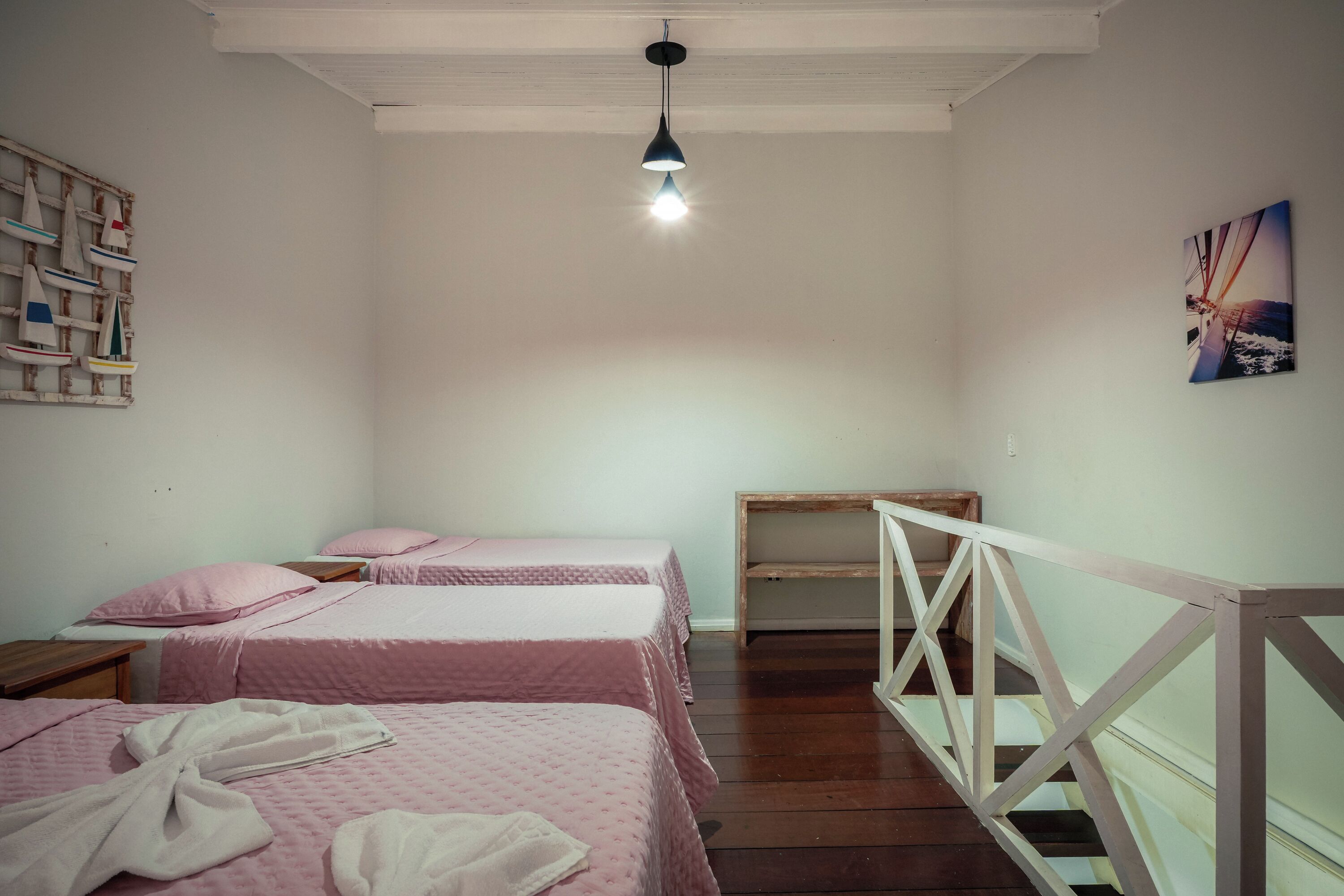 Ein Zimmer mit zwei Betten, Holzboden, einer weißen Geländer und einer Pendelleuchte.
