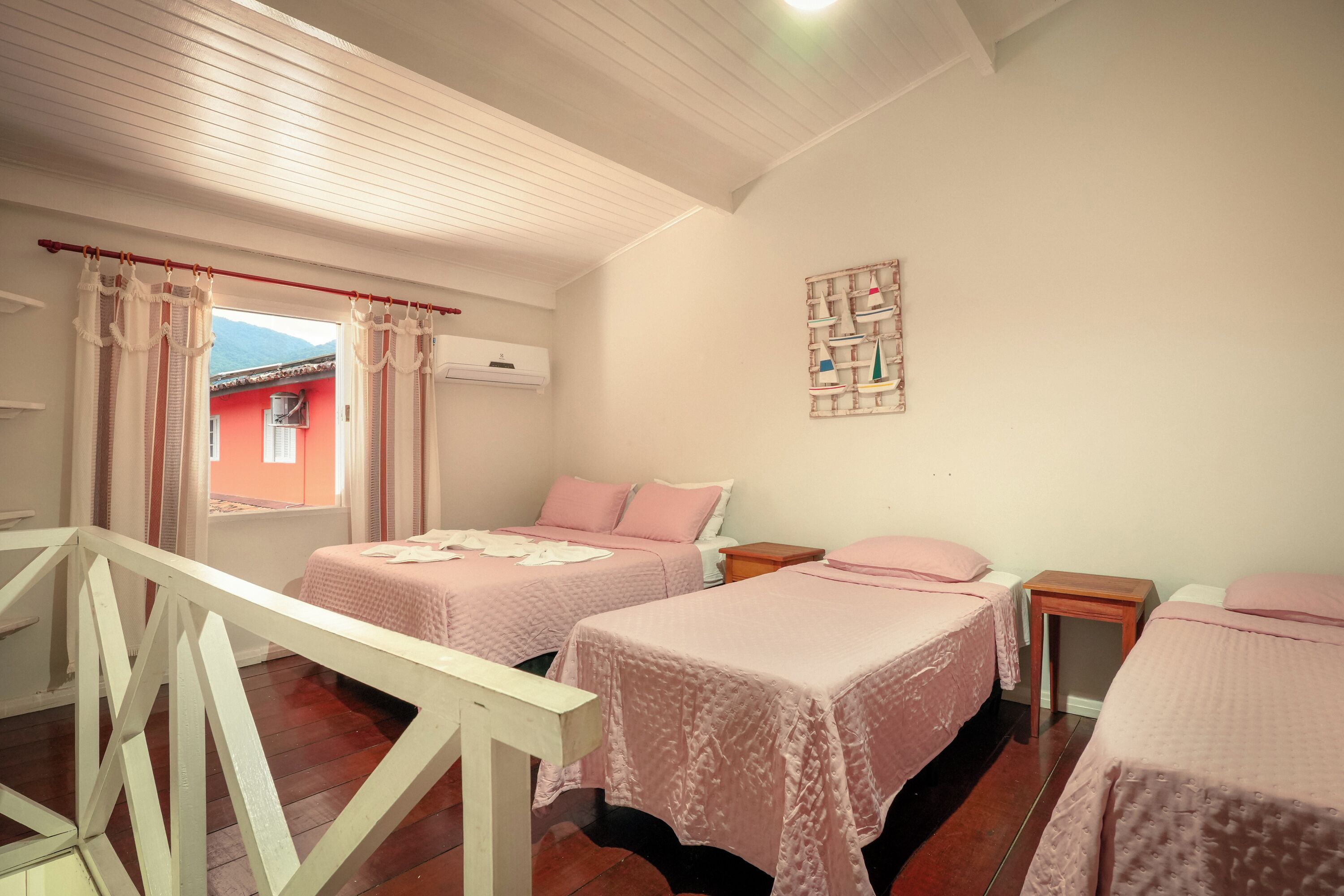 Een slaapkamer met twee bedden, een houten leuning, een klein tafeltje en een wandplank met decoratieve spullen.