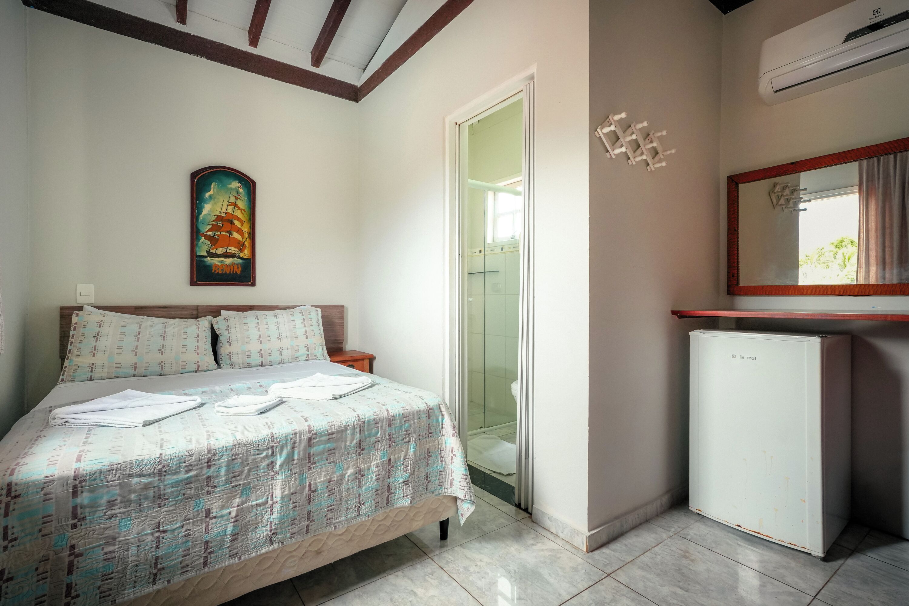Habitación con cama, un refrigerador pequeño, zona de ducha y aire acondicionado de pared.