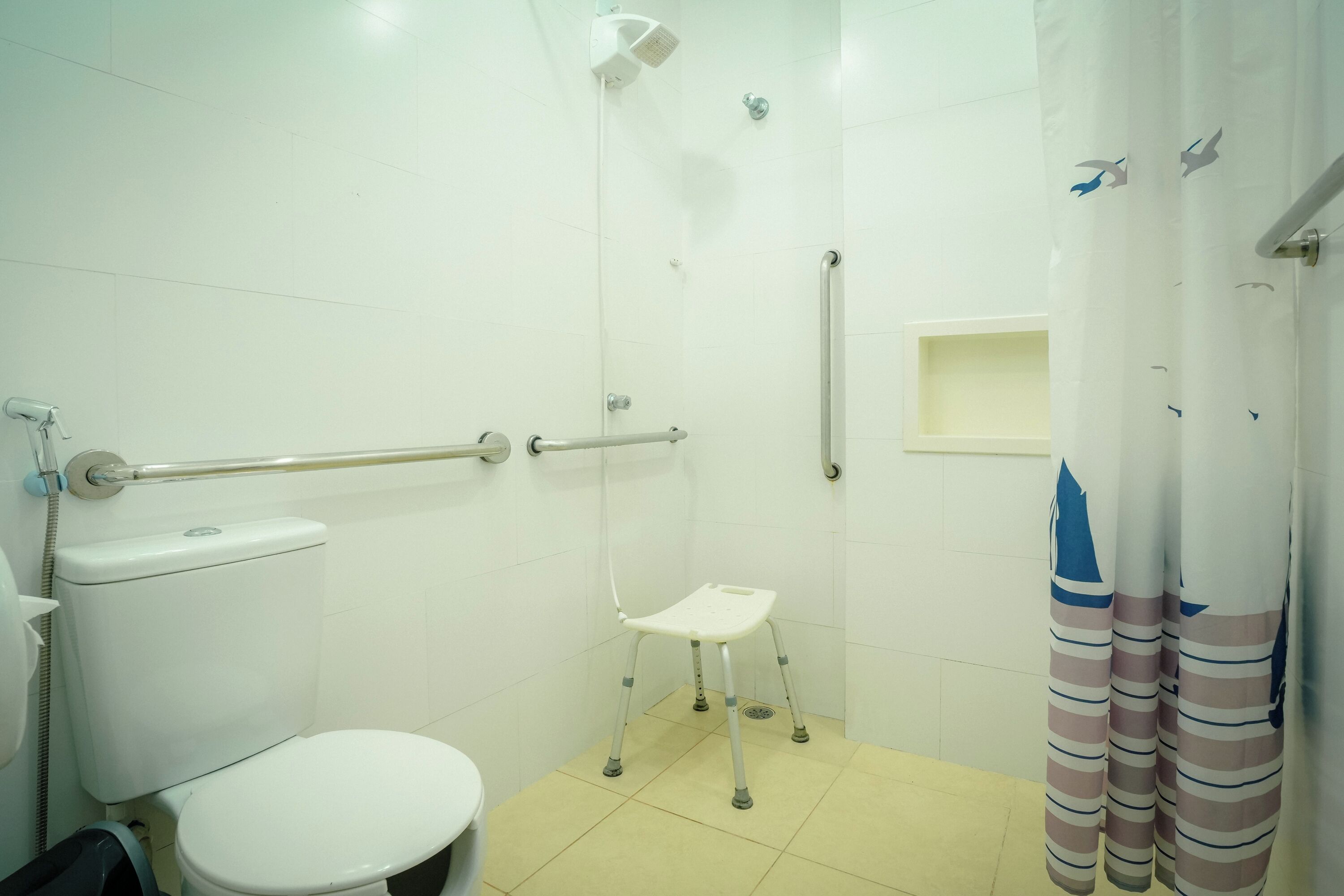 A small, clean bathroom with a toilet, a shower, and a grab bar for support.