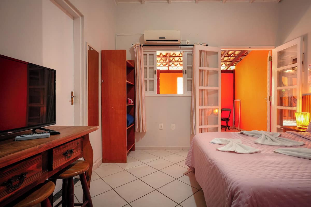 Une chambre d’hôtel avec un lit, un bureau avec une télévision, une armoire et une fenêtre avec des rideaux.