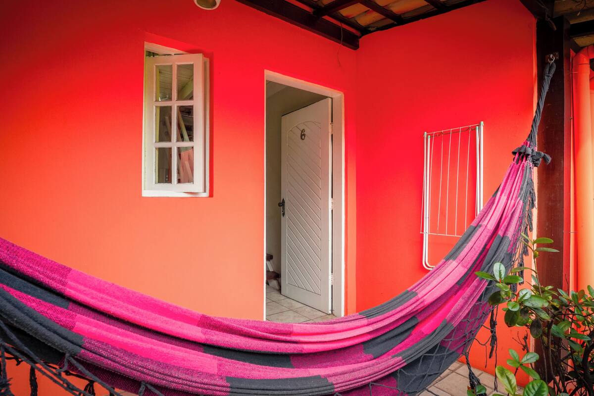 Un bâtiment rouge avec une porte et une fenêtre blanches, un hamac et un étendoir en métal.