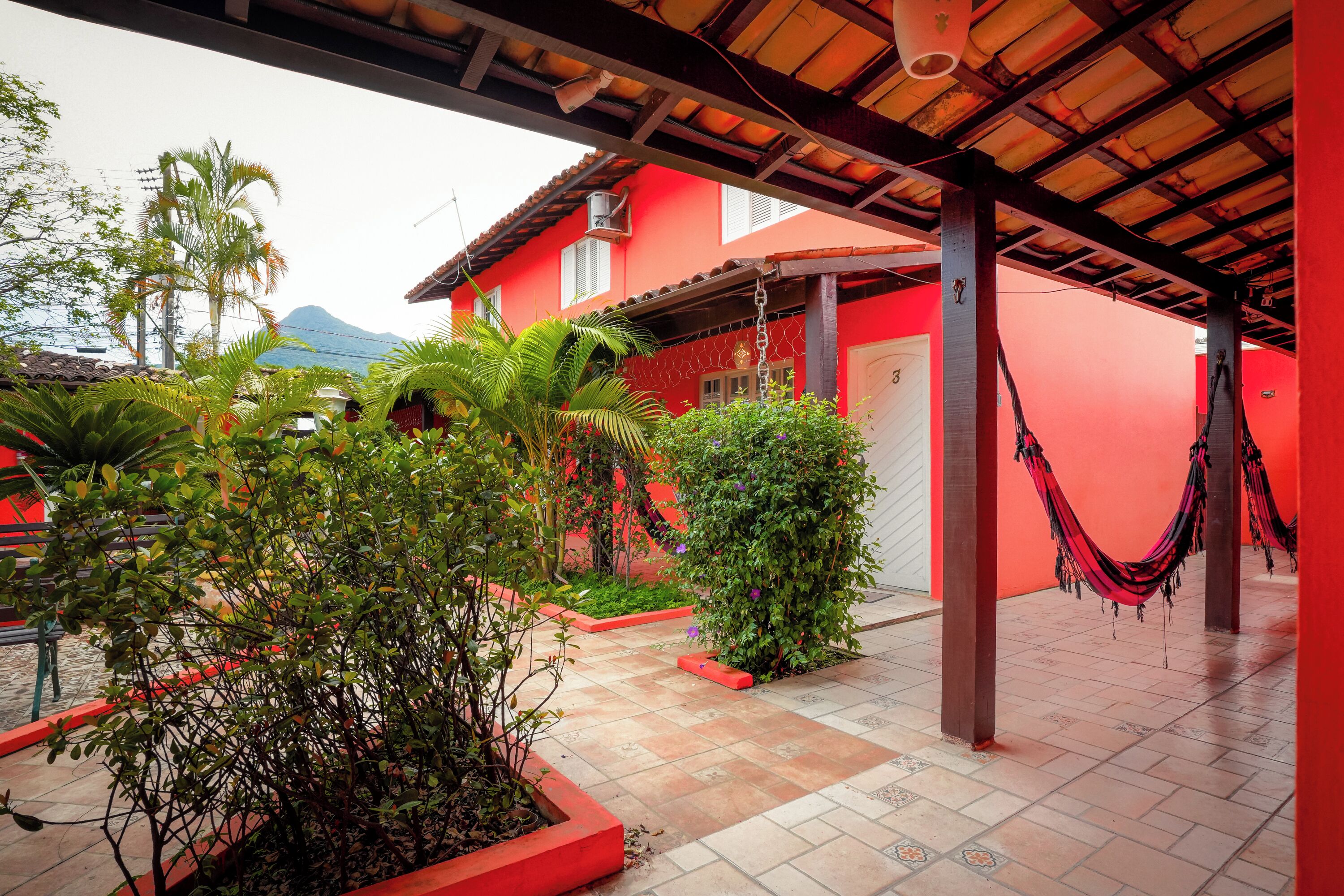 A red building with a covered patio area, surrounded by greenery and a hammock.