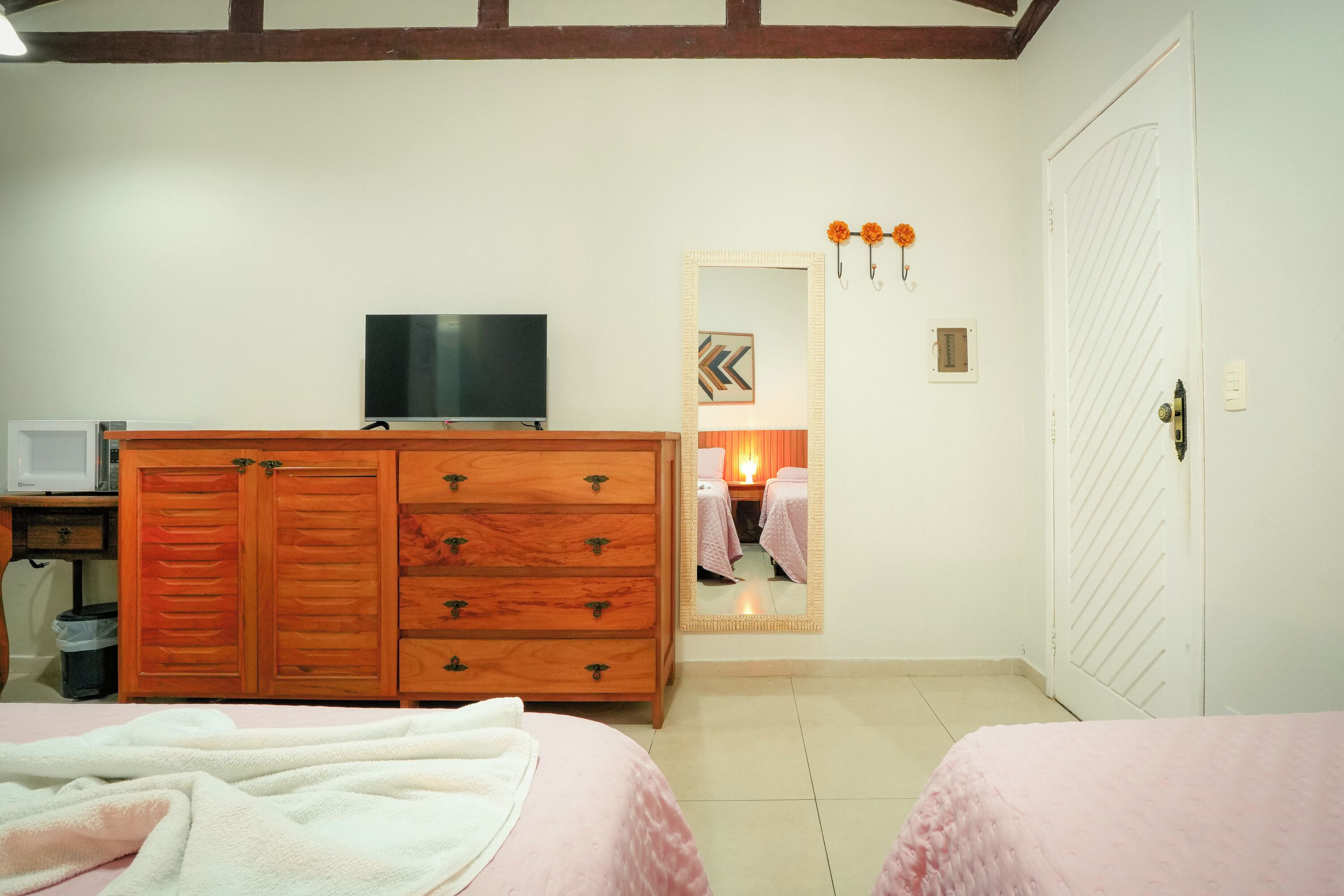 Un dormitorio con dos camas, un aparador de madera, un televisor y una puerta blanca.