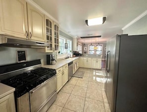 A modern kitchen with stainless steel appliances, light-colored cabinetry, and a tiled floor.