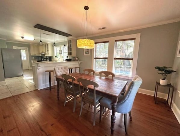 A spacious kitchen with a central island, wooden dining table with chairs, and large windows providing natural light.