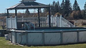An above-ground swimming pool with a covered seating area and a white fence.