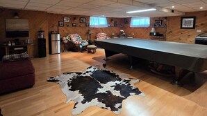 A spacious room with a pool table, wooden flooring, and a cowhide rug.